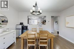 Open concept dining area featuring wood-finish flooring, a contemporary chandelier, a pass-through window to the kitchen, and a neutral color palette - 