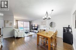 Open-concept living and dining area featuring wood-finish flooring, a contemporary chandelier, and a large window - 