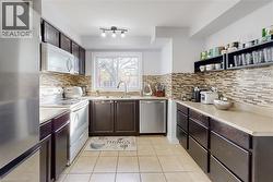 Kitchen featuring dark wood-finish cabinetry, light-toned countertops, and a full tile backsplash - 