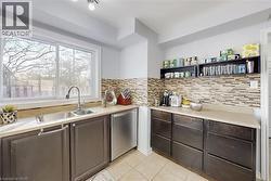 Kitchen featuring a dual basin stainless steel sink with a high-arch faucet, a large sliding window, textured tile backsplash, dark wood-finish cabinetry, and stainless steel appliances - 