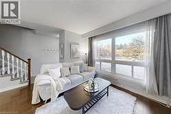 Living area featuring large multi-pane window, wood-finish flooring, light grey walls, and a staircase with white spindles and a wood handrail - 