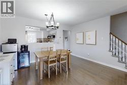 Open-concept living area featuring wood-finish flooring, a contemporary chandelier, and a staircase with white balusters - 