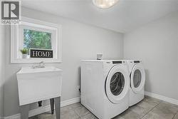 Dedicated laundry area featuring a utility sink with dual-handle faucet, window with white trim, and tile flooring - 