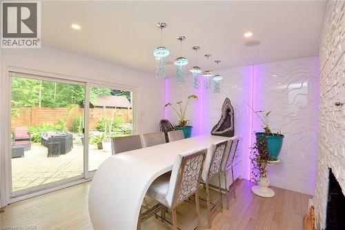 Modern dining area featuring a curved white table, unique pendant lighting, and an accent wall with textured panels and recessed lighting - 4299 Lakeshore Road, Burlington, ON - Indoor