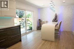 Contemporary dining area featuring a curved white dining table, light wood-finish flooring, and a unique wall panel with integrated backlighting - 