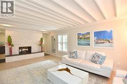 Living space featuring a white stacked stone fireplace with a black hearth, light wood-finish flooring, and white coffered ceilings - 