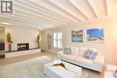 Living space featuring a white stacked stone fireplace with a black hearth, light wood-finish flooring, and white coffered ceilings - 4299 Lakeshore Road, Burlington, ON - Indoor Photo Showing Living Room With Fireplace