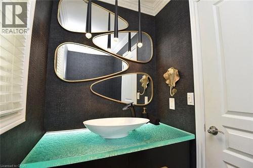 Powder room featuring a vessel sink atop a translucent countertop, dark textured wallpaper, and gold-framed mirrors - 4299 Lakeshore Road, Burlington, ON - Indoor Photo Showing Bathroom