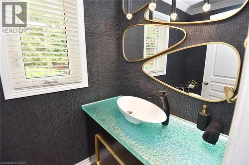 Powder room featuring a unique textured dark wall covering, a clear glass vanity top with integrated lighting, and a white vessel sink with a black faucet - 4299 Lakeshore Road, Burlington, ON - Indoor Photo Showing Bathroom