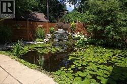 Outdoor koi pond featuring a rock waterfall, surrounding stone paving, and a rich wooden privacy fence - 