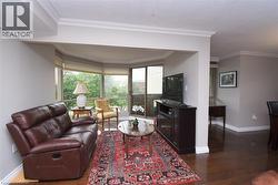 Living area featuring a bay window with multiple panes, dark wood-finish flooring, and crown molding - 