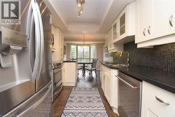 Galley kitchen featuring stainless steel appliances, dark stone countertops, white cabinetry, a tiled backsplash, and recessed lighting - 