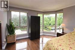 Room featuring expansive bay windows, rich wood-finish flooring, crown molding, and a neutral wall palette - 