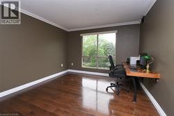 Spacious room featuring rich wood-finish flooring, a large window, crown molding, and a built-in wall-mounted desk - 