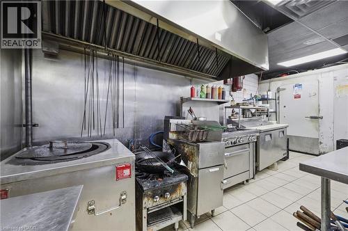 Commercial kitchen featuring stainless steel appliances, a large exhaust hood system, tile flooring, and a walk-in cooler - 239 York Boulevard, Hamilton, ON 