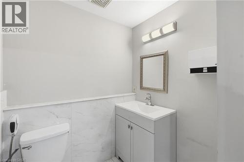 Modern bathroom featuring a single vanity with a white countertop and base cabinet, a rectangular framed mirror, and a wall-mounted light fixture - 239 York Boulevard, Hamilton, ON 