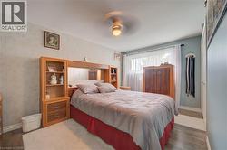 Bedroom featuring wood-finish flooring, light blue and patterned walls, a ceiling fan with integrated lighting, and a large window with sheer white curtains - 