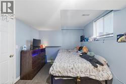 Bedroom featuring light blue walls, wood-finish flooring, and a large window with blinds - 