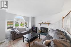 Living room featuring vaulted ceilings, a large arched window, a fireplace with a tiled hearth, and a wood-finish staircase railing - 