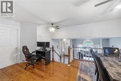 Upper-level space featuring wood-finish flooring, a white paneled door, and a ceiling fan - 