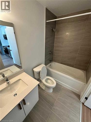 Bathroom featuring a full bathtub with tiled surround, a vanity with a white countertop and integrated sink, a toilet, and wood-finish flooring - 2782 Barton Street E, Hamilton, ON 