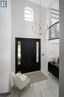 Grand entryway featuring a soaring ceiling, an arched transom window, a two-story gold-finish chandelier, a black paneled door with glass sidelights, and large-format tile flooring - 