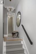 Staircase featuring herringbone pattern carpet runner, white risers, and a matte black wall-mounted handrail - 