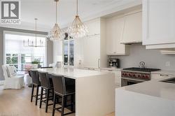 Gourmet kitchen featuring a large central island with seating, integrated appliances, white cabinetry, professional-grade range, and light wood-finish flooring - 