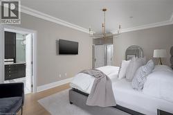Spacious room featuring light wood-finish flooring, a contemporary gold-tone chandelier, and crown molding - 
