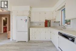 Kitchen featuring white cabinetry, light-toned countertops, a stainless steel sink with a single-handle faucet, and light wood-finish flooring - 