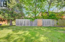Expansive green lawn bounded by a natural wood fence with a single wood gate, all surrounded by mature trees - 