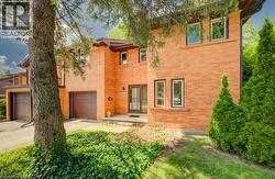 Brick exterior featuring a covered entry, multiple windows with dark trim, an attached garage with a brown panel door, and mature landscaping - 