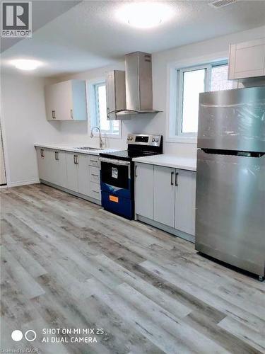 Kitchen featuring wood-finish flooring, white cabinetry, integrated sink, stainless steel appliances, and abundant natural light from multiple windows - 389 Tealby Crescent Unit# Lower, Waterloo, ON 