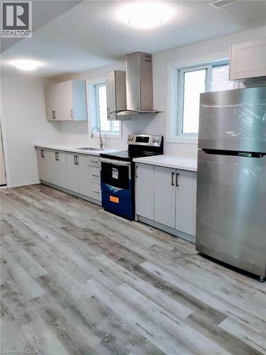 Contemporary kitchen featuring wood-finish flooring, white cabinetry, light countertops, and stainless steel appliances including a range hood, stove, and refrigerator - 389 Tealby Crescent Unit# Lower, Waterloo, ON 