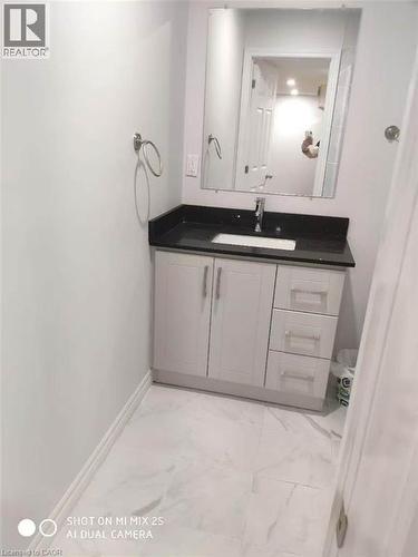Bathroom featuring a white vanity with panel cabinetry and drawer storage, a dark countertop with an integrated sink, a rectangular wall-mounted mirror, and large format floor tiling - 389 Tealby Crescent Unit# Lower, Waterloo, ON 
