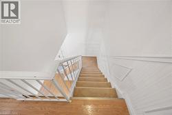 Staircase featuring carpeted treads, a white metal railing, and wood-finish flooring at the landing - 