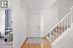 Entryway featuring wood-finish flooring, white paneled door with sidelight, carpeted staircase with white railing, and white wainscoting - 