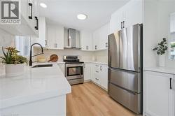 Modern kitchen featuring white cabinetry, stainless steel appliances, light wood-finish flooring, white countertops, and a subway tile backsplash - 
