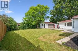 Expansive backyard featuring a large grass area, mature trees, a detached two-car garage with red roofing, a single-car garage, and a concrete patio - 