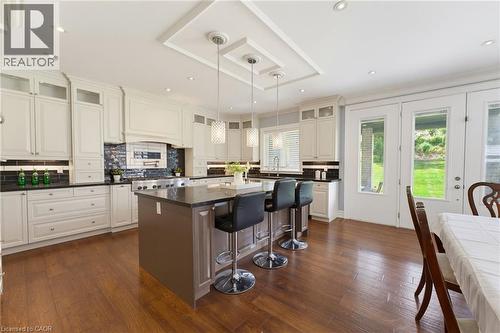 Gourmet kitchen featuring a large central island with seating, dark wood-finish flooring, white cabinetry, dark countertops, and a subway tile backsplash - 38 River Valley Drive, Kitchener, ON 