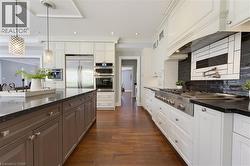 Gourmet kitchen featuring a large central island with dark cabinetry, professional-grade stainless steel appliances including a double oven and refrigerator, a gas range with a pot filler, and contras - 