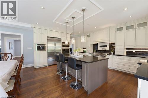 Gourmet kitchen featuring a large island with seating, stainless steel appliances, extensive white cabinetry, dark countertops, and wood-finish flooring - 38 River Valley Drive, Kitchener, ON 