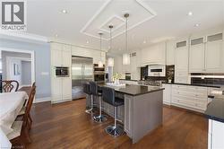 Gourmet kitchen featuring a large island with seating, stainless steel appliances, extensive white cabinetry, dark countertops, and wood-finish flooring - 