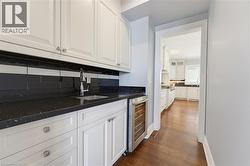 Wet bar featuring white shaker cabinetry, black speckled countertops, a stainless steel undermount sink with a gooseneck faucet, black subway tile backsplash, and an integrated beverage refrigerator - 