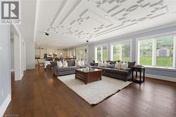 Expansive living area with wood-finish flooring, an intricate coffered ceiling, and recessed lighting - 