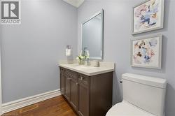Powder room featuring a dark wood-finish vanity with a light-toned countertop, a rectangular mirror, a white toilet, and wood-finish flooring - 