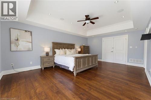 Spacious bedroom featuring wood-finish flooring, a tray ceiling with a ceiling fan, recessed lighting, and double panel doors - 38 River Valley Drive, Kitchener, ON 