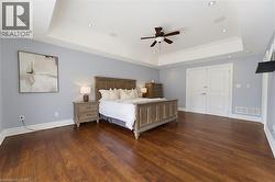 Spacious bedroom featuring wood-finish flooring, a tray ceiling with a ceiling fan, recessed lighting, and double panel doors - 