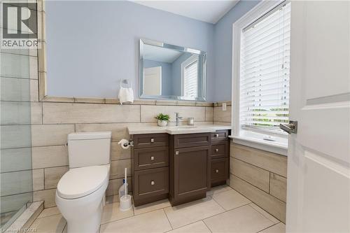 Bathroom featuring a single vanity with a white countertop, a rectangular mirror, a window with horizontal blinds, and a tiled shower enclosure - 38 River Valley Drive, Kitchener, ON 