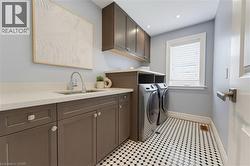 Laundry area featuring dark cabinetry, light countertops, a sink with a gooseneck faucet, window with blinds, and geometric black and white floor tiling - 
